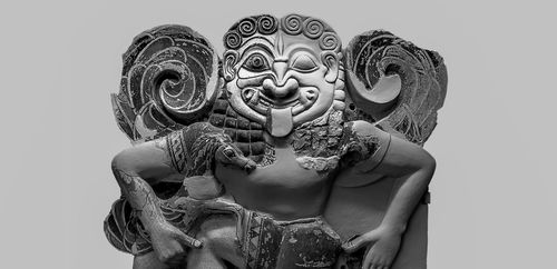 Fotografia in
bianco e nero di un'antica scultura in terracotta raffigurante una figura
simile a una gorgone, con un viso ghignante, lingua sporgente e grandi
elementi decorativi a spirale ai lati, mentre tiene degli animali tra le
braccia.